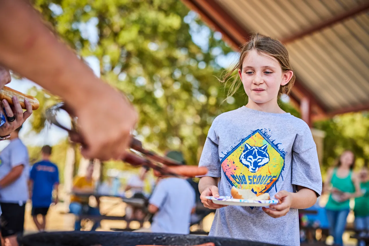 A Cub Scout prepares food at an outdoor cookout