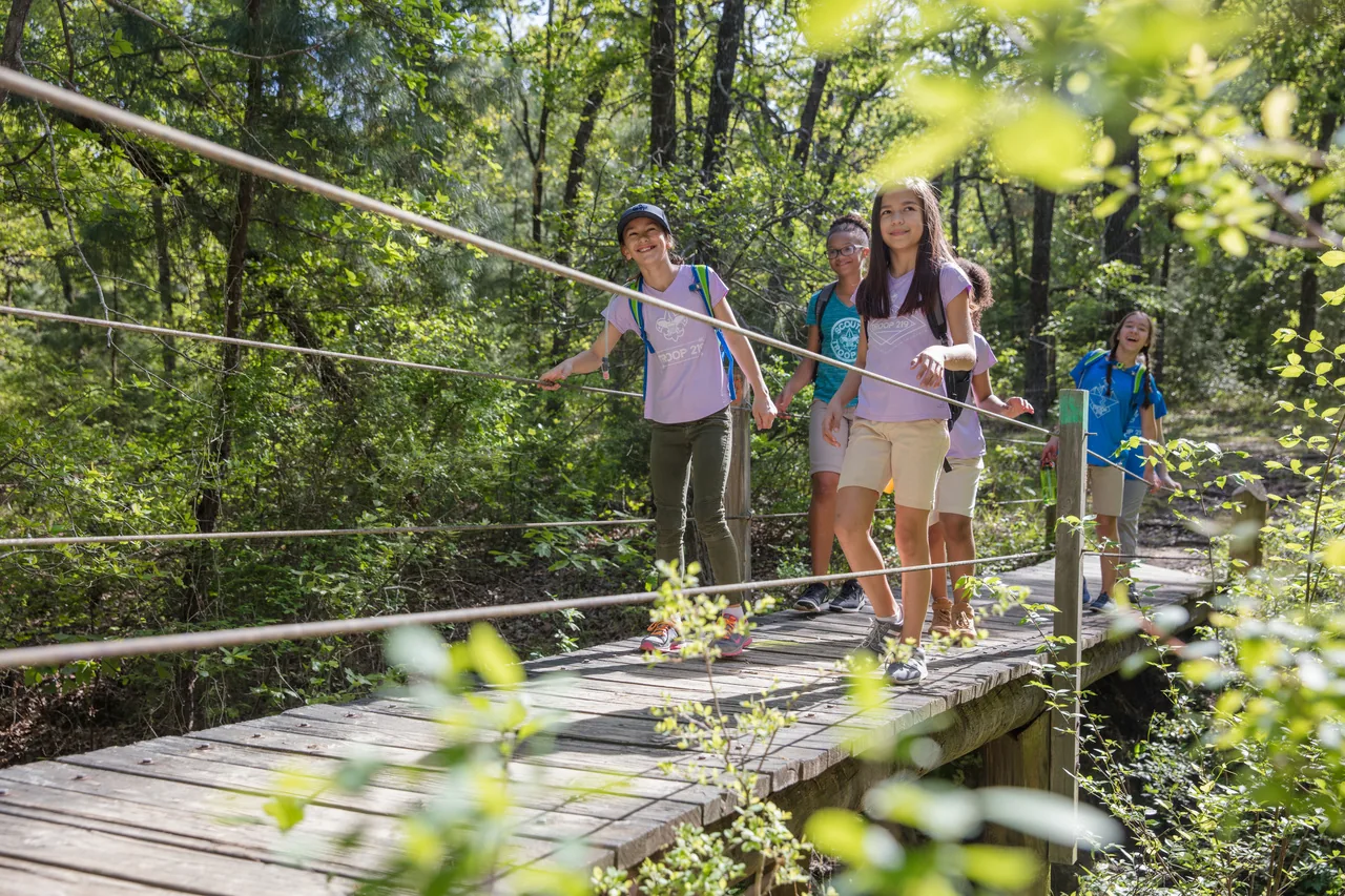 Girls in Scouts BSA hike together across a wooded footbridge